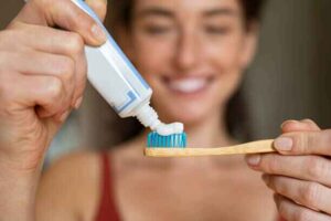Woman smiling confidently while holding a tube of nano-hydroxyapatite toothpaste, a safe alternative for enamel repair.